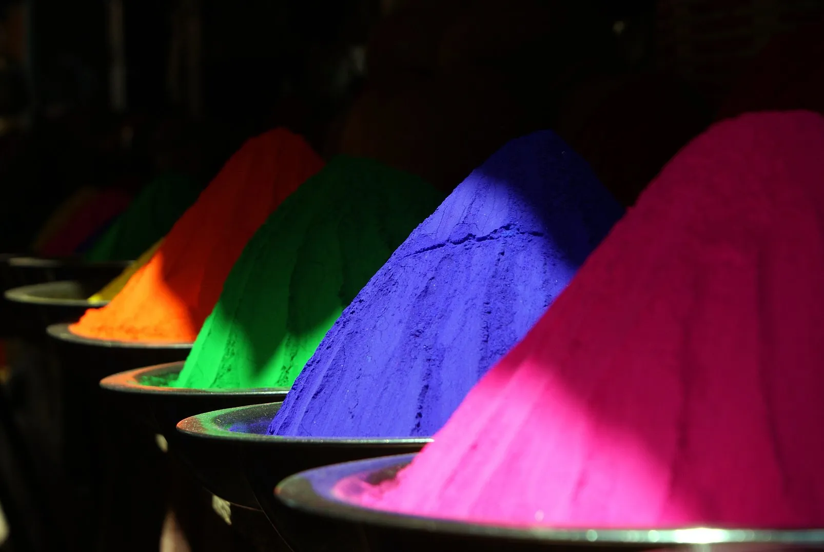 Farbpigmente als Pulverkegel in Orange, Grün, Blau und Pink