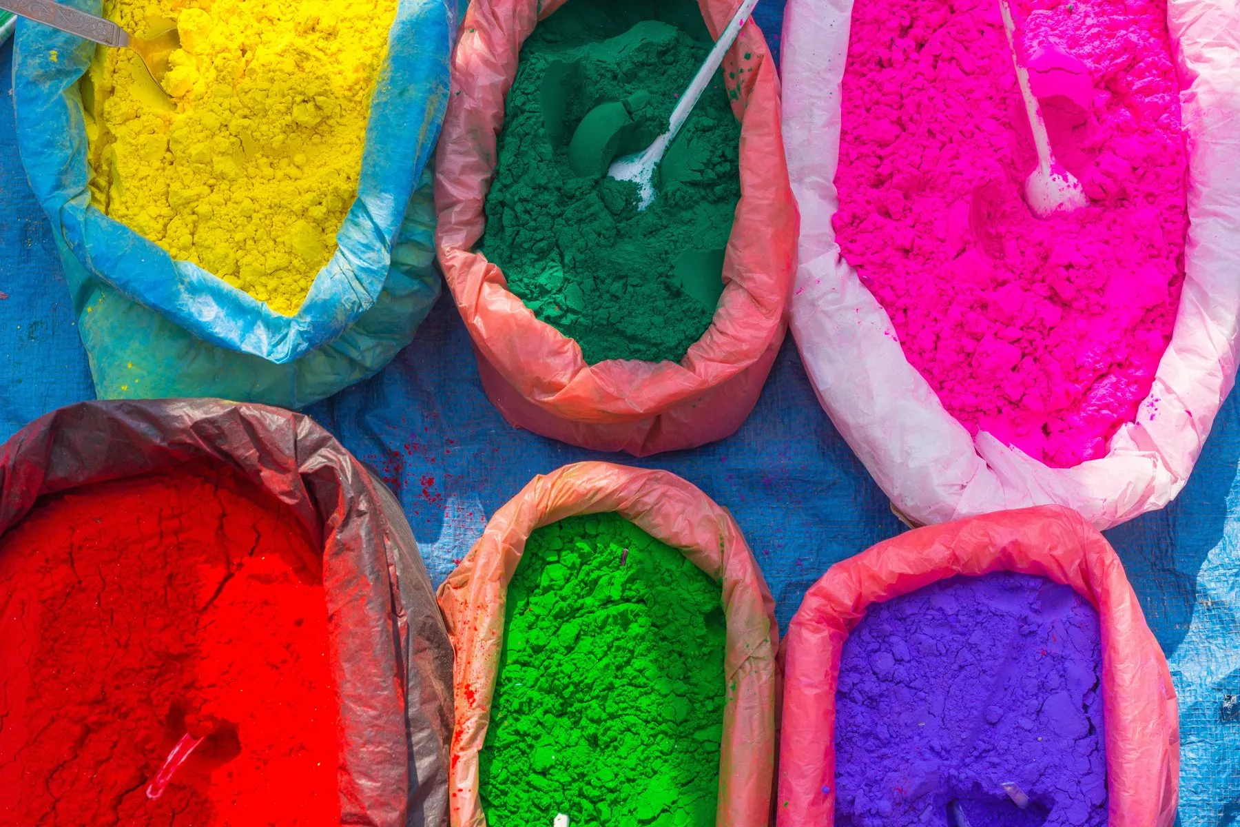 Säcke mit leuchtend farbigem Pulver in Gelb, Grün, Pink, Rot und Violett