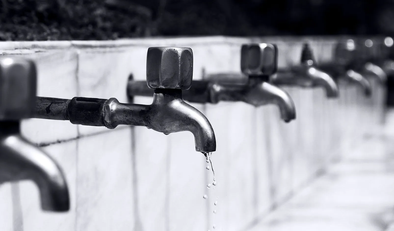 Reihe von Wasserhähnen, aus einem tropft Wasser